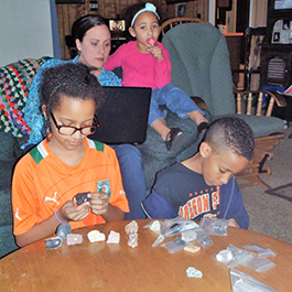 Carol works on a geology assignment in her living room while her three children experiment with the rocks in the lab kit.