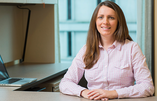 Kathleen Garney, an Ecampus student in the MBA in Executive Leadership track, sits at a desk with her hands resting atop it. 