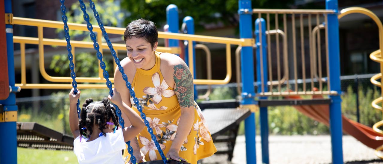 Woman in yellow dress pushing young child on a tire swing at children's playground
