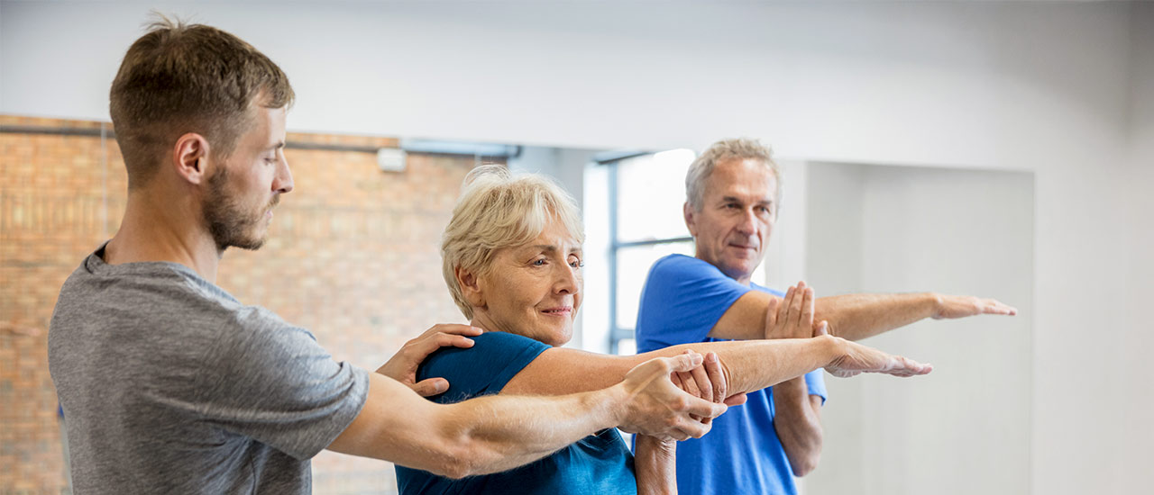 Older couple stretching their upper torsos with support from a younger male physical therapist