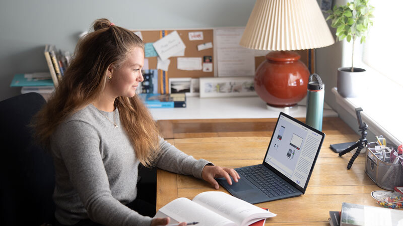 A photo of Fiona Wylde seated at a desk, reading a laptop with a nearby book open.