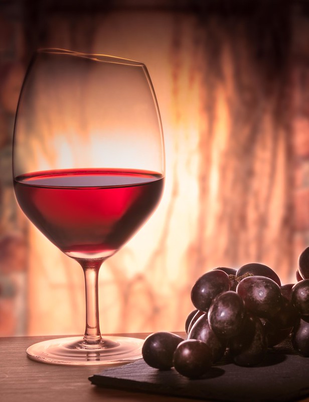 A glass of red wine and bunch of grapes in low light.