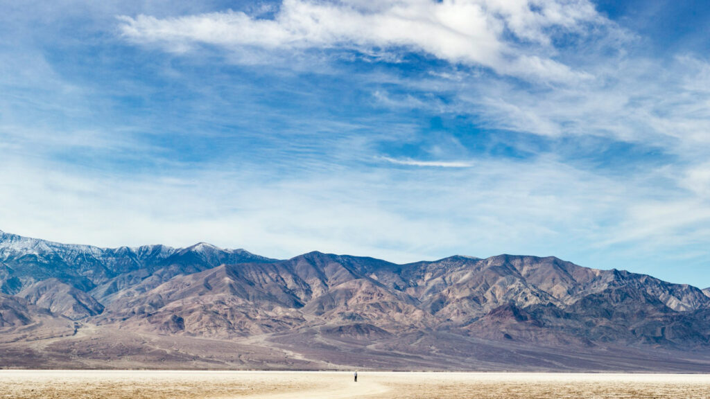 Panoramic photo of a lone person standing in the vast landscape of Bad Water Basin in Death Valley National Park in California.