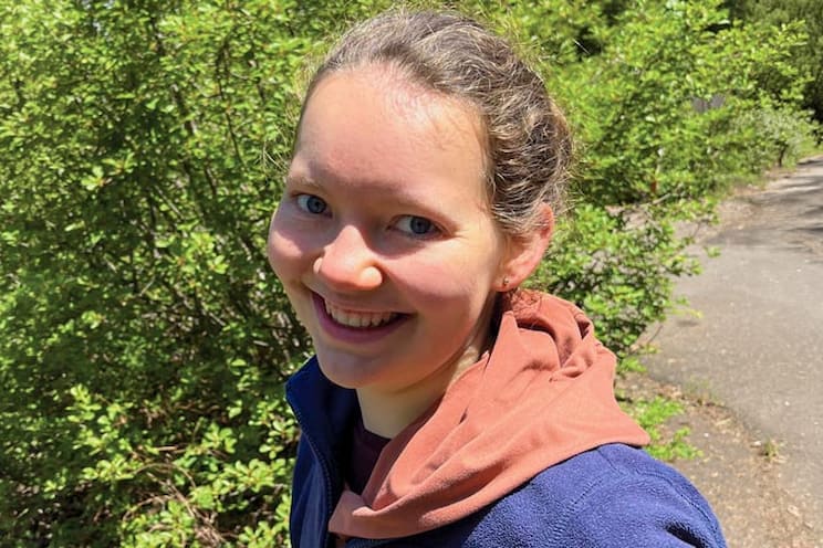 Oregon State University student Kari Shippen outdoors on a sunlit trail, with greenery and a path in the background