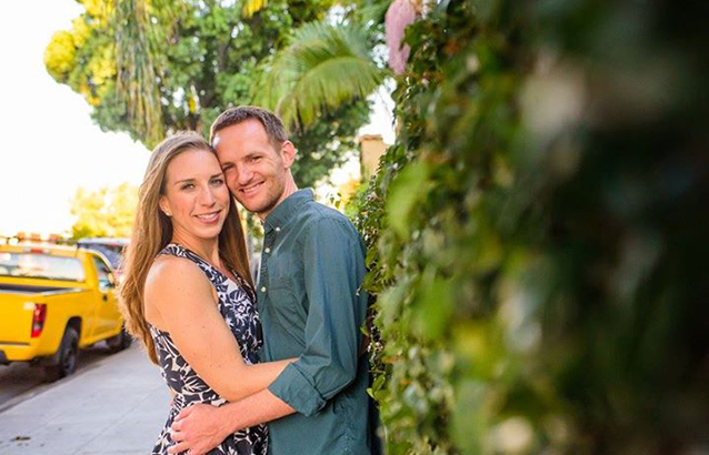 Ryan Fox and his fiancée, Liz, pose with their arms around each other near a tall hedge.