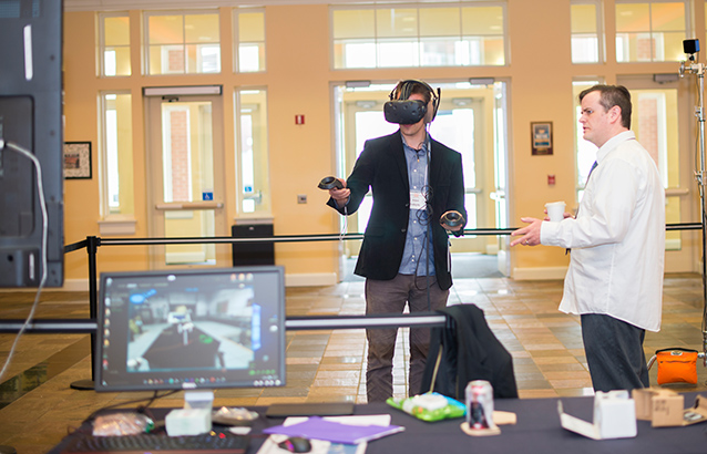 Warren Blyth helps an Ecampus instructor use a virtual reality headset and controls in an educational setting.