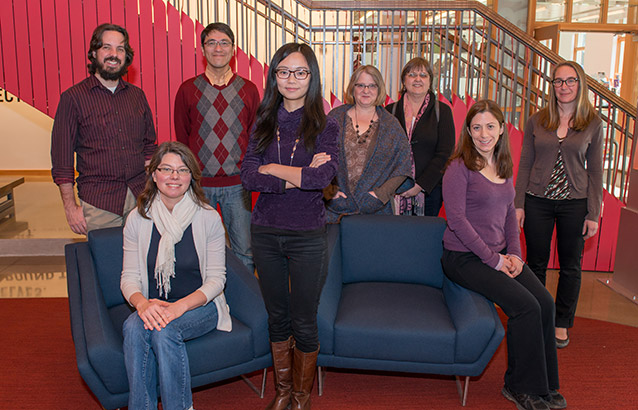 The eight inaugural Ecampus Research Fellows stand and sit together in the Student Experience Center.
