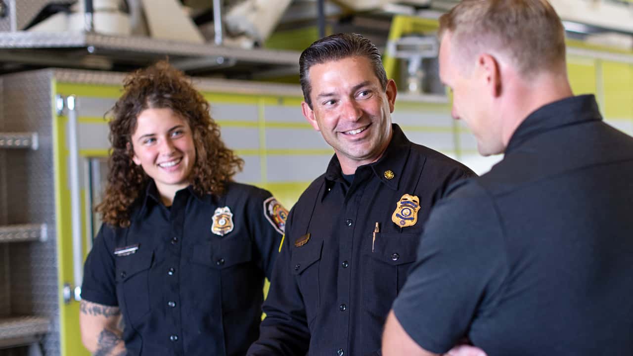 Bob Horton smiles as he converses with two firefighter colleagues in a fire station