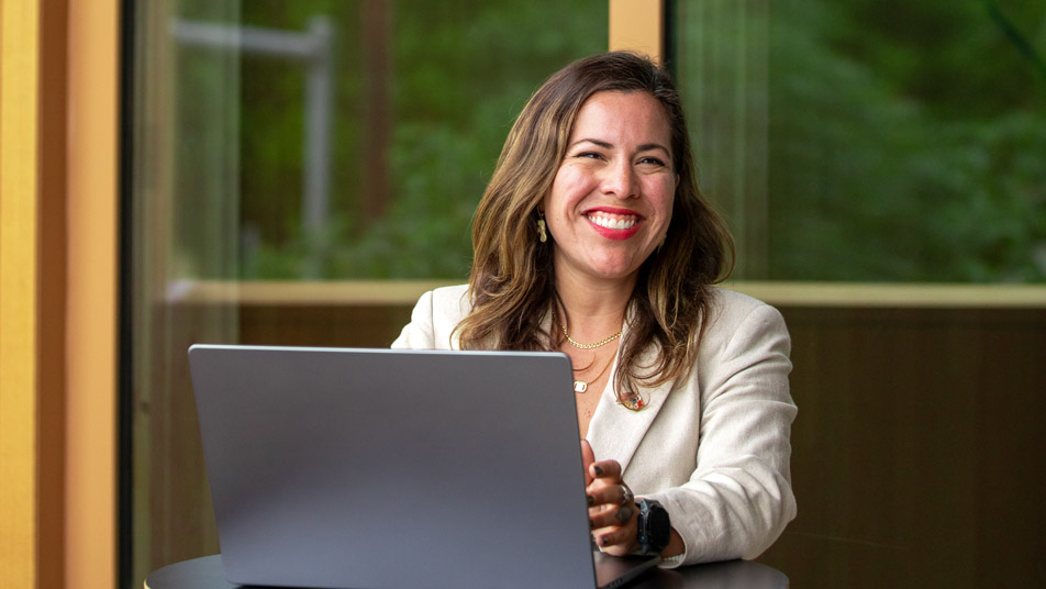 Carla Perscky, an Oregon State University environmental sciences graduate, smiles while sitting at a table in front of big windows.