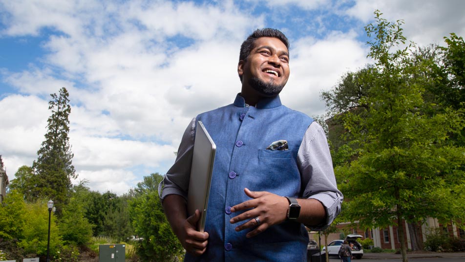 Patric Papabathini, an Oregon State University Ecampus graduate who earned a bachelor’s degree in business administration, stands smiling while holding his laptop.