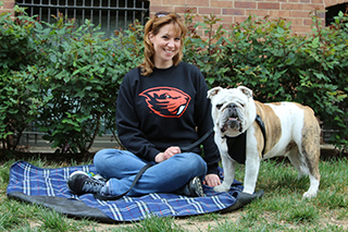 Christine Mosser sits on a blue blanket spread out on the lawn and her bulldog, Chesty, stands next to her. 