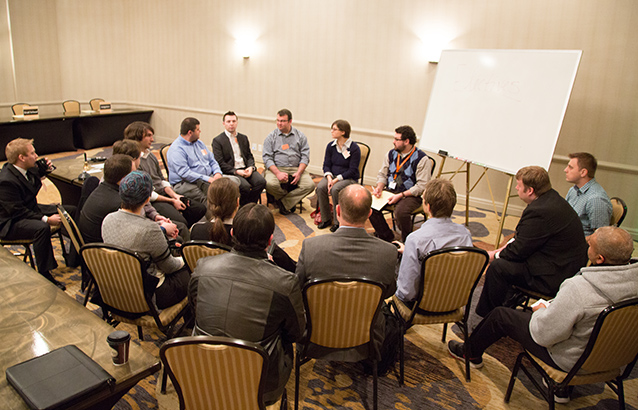 A group of seventeen post-baccalaureate computer science students are seated in a loose circle, discussing benefits, questions and concerns regarding the online program with faculty members at the Computer Science Career Showcase.