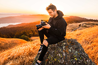 Jake Chamseddine, digital communication arts graduate, sitting on a rock with the sunset behind him