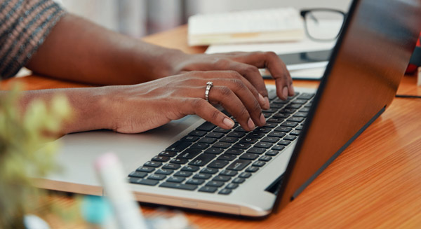Hands typing on a laptop keyboard at a desk.