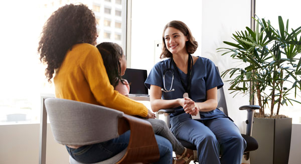 Two people sit with a healthcare professional in a bright office, having a conversation during a medical or counseling appointment.
