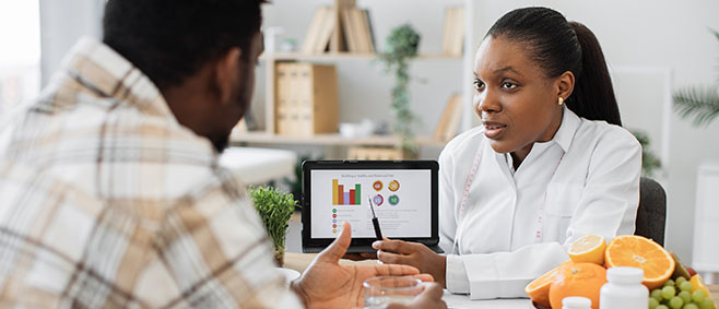 Nutritionist reviewing health charts on a tablet with a patient discussing healthy eating choices at a consultation table.