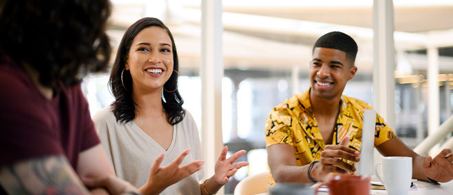 Woman speaking with hand gestures during a group discussion while others listen and respond around a table.