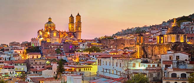 Vibrant hillside town in Mexico with colorful homes and a glowing cathedral at sunset