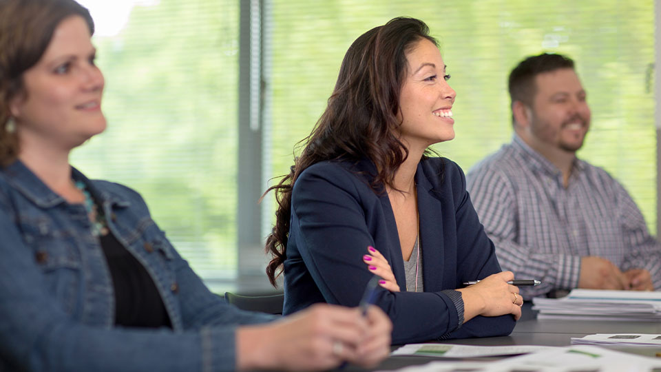 Veronica Garcia wears a blue blazer and sits in a row with two classmates while listening to an out of frame instructor.