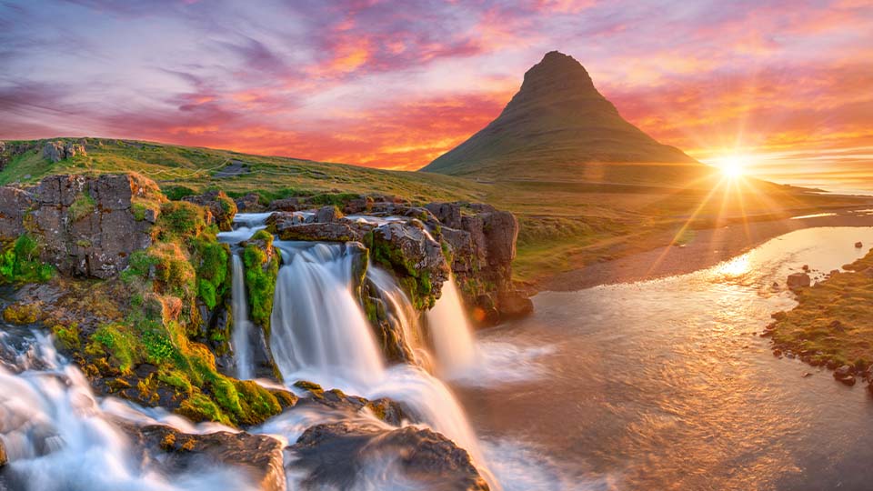 A panoramic view of Mt. Kirkjufell, a mountain in Iceland, accompanied by nearby waterfalls, near the Icelandic coast
