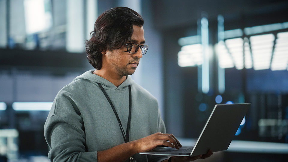IT professional standing with a laptop, focused on work in a technology-focused office setting.