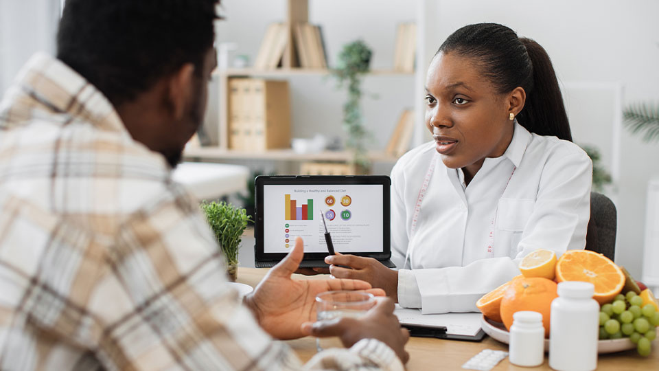 Nutritionist reviewing health charts on a tablet with a patient discussing healthy eating choices at a consultation table.