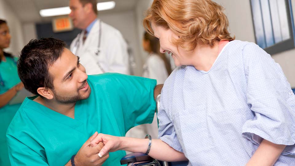 Middle-aged, female patient in wheelchair holding hand of male nurse in green scrubs
