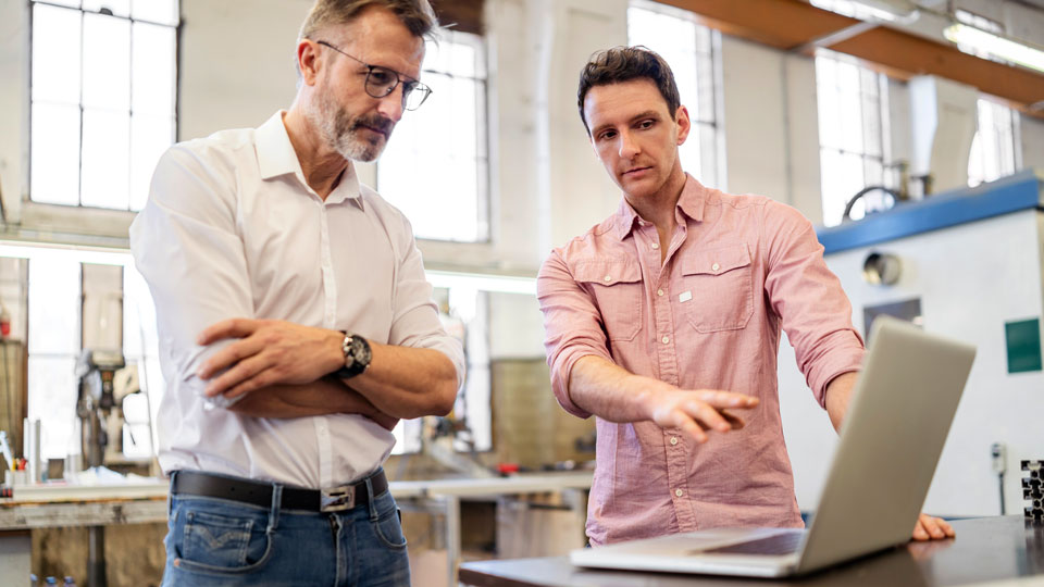 Two men in a workshop, one pointing at a laptop