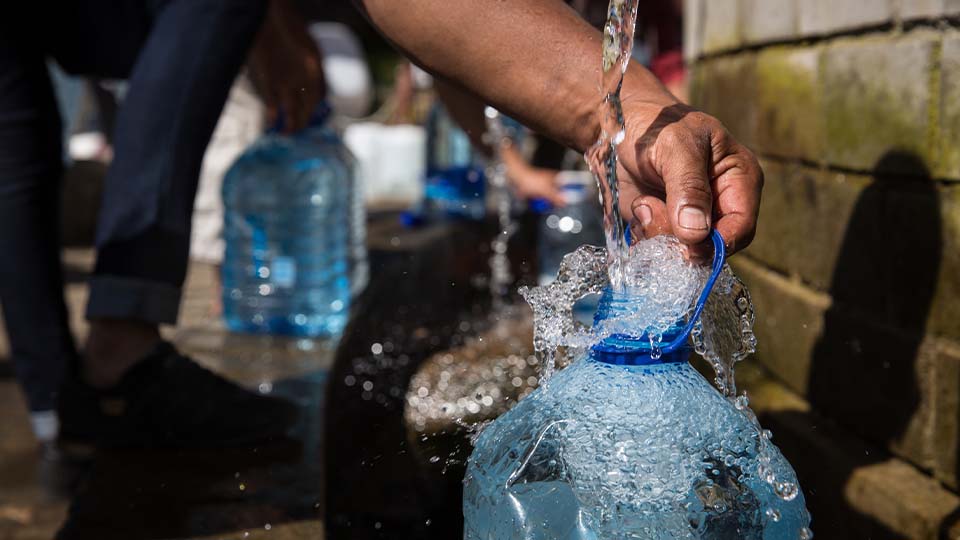 A close up of someone filling a 3-gallon jug with clean drinking water. Several people in the background are doing the same.