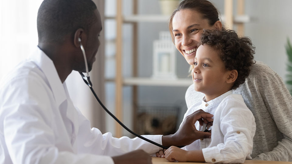 A woman smiles at a doctor while the happy child on her lap gets a medical exam