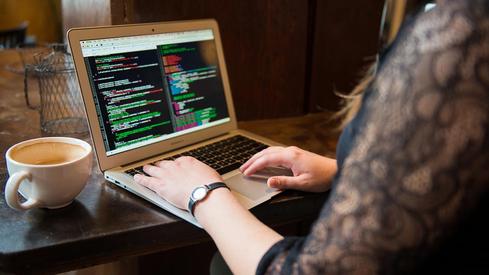 Woman reviewing code on laptop computer with cup of coffee