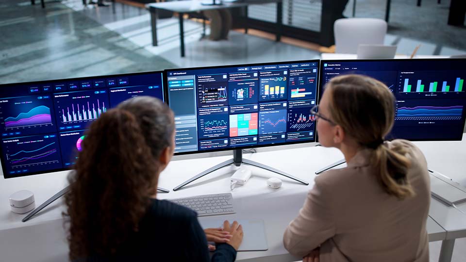 Two professionals reviewing dashboards on dual monitors, collaborating to analyze data trends and insights