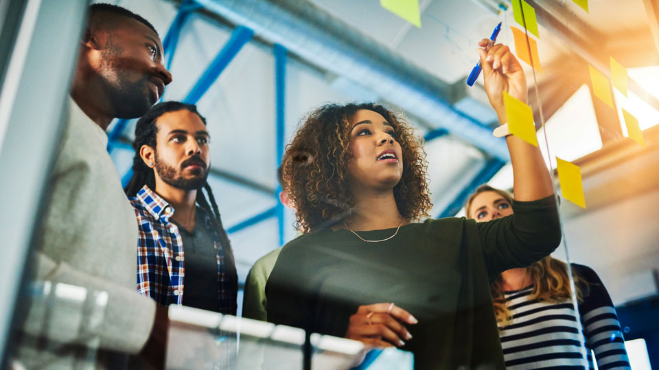 A diverse group of young professionals collaborates with sticky notes in a modern office.