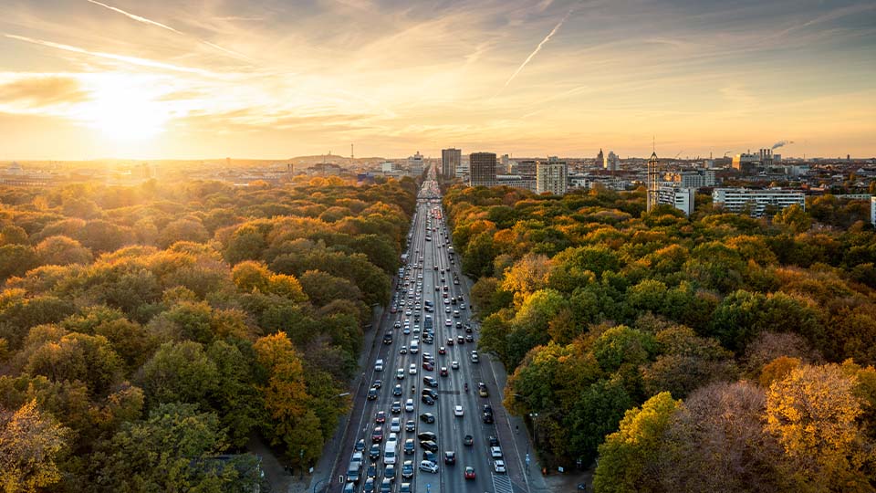 Massive roadway with cars splitting a wooded area with deciduous trees and a small city to the east