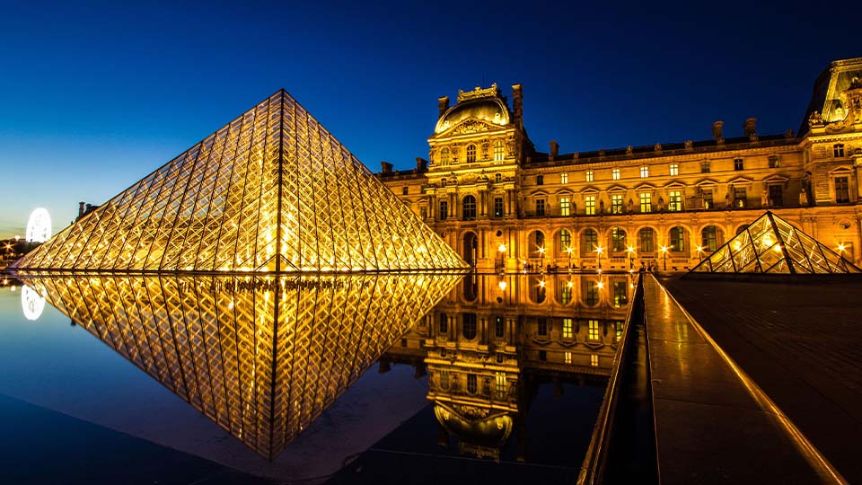 Musée du Louvre illuminated at night with pyramid in foreground reflecting in water