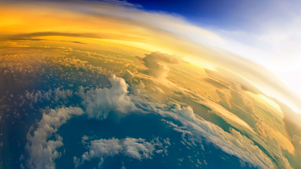 A curved aerial view of Earth's atmosphere with golden sunlight and clouds