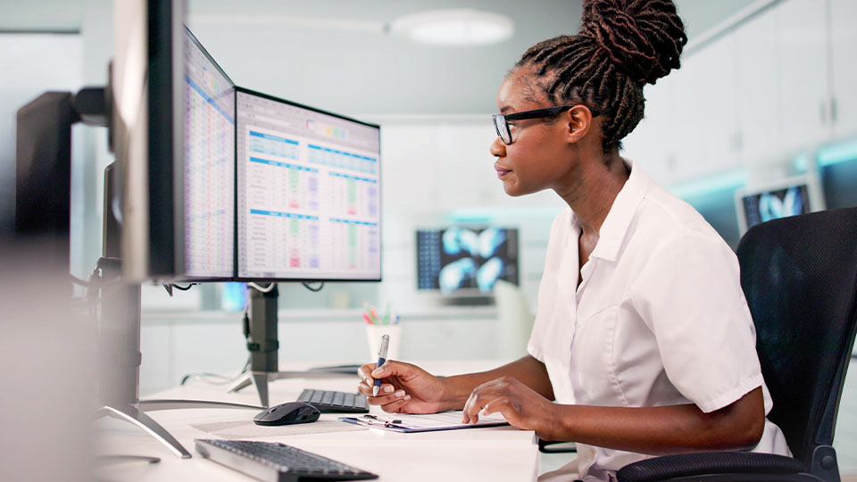 A health care administrator working at a desk with computer monitors displaying data charts