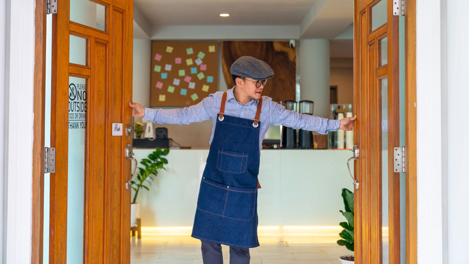 A man in an apron and cap holds open two wooden doors in a modern building