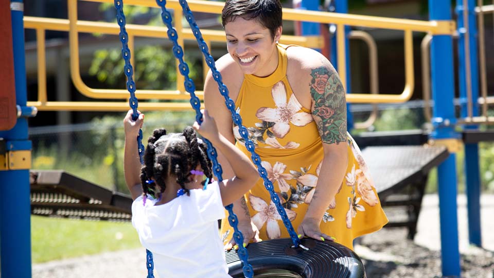 Woman in yellow dress pushing young child on a tire swing at children's playground