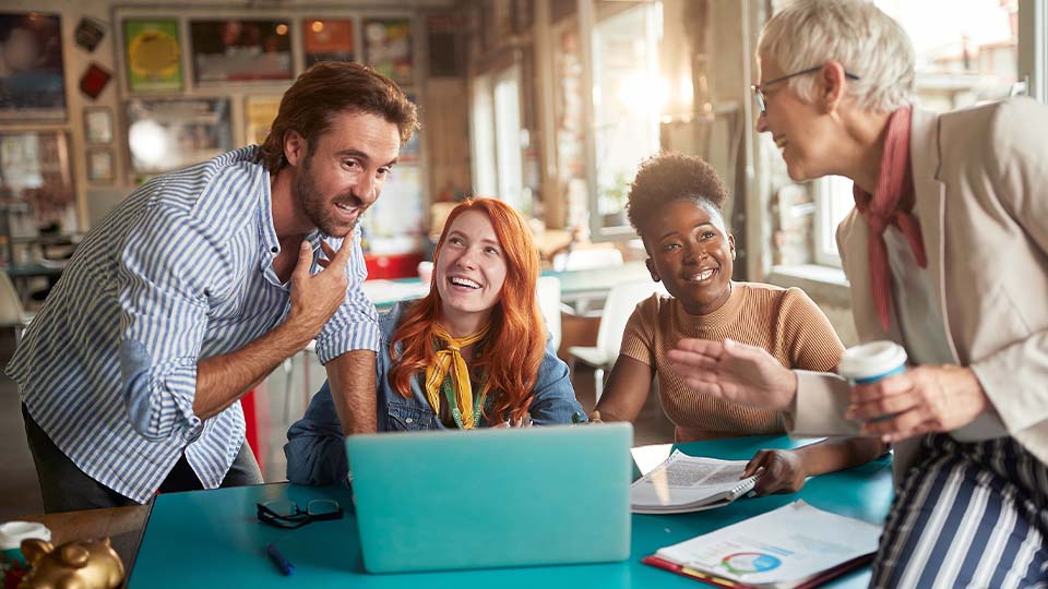 Group of business professionals smiling and collaborating around a laptop in a modern office setting with creative energy