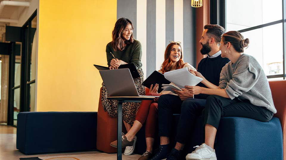 Four professionals collaborate and share ideas with papers and a laptop in a modern, creative workspace