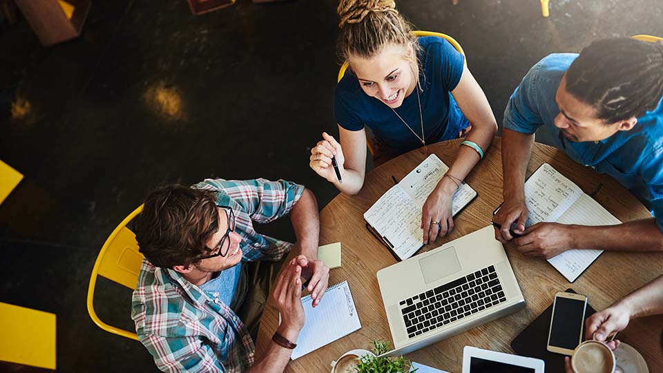 Group of people in discussion around a circular table with open notebooks and pens