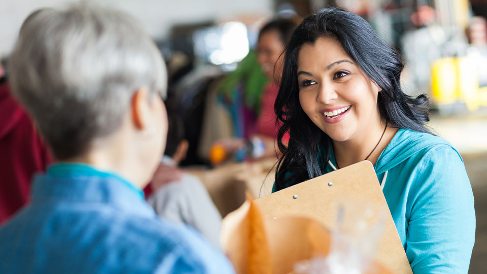 Young woman with clipboard smiling at woman holding a paper bag