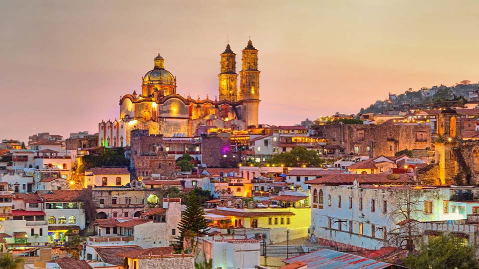 Vibrant hillside town in Mexico with colorful homes and a glowing cathedral at sunset