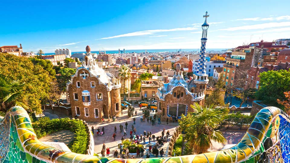 Colorful tile wall in foreground of Parc Güell in Barcelona with brightly colored buildings in background