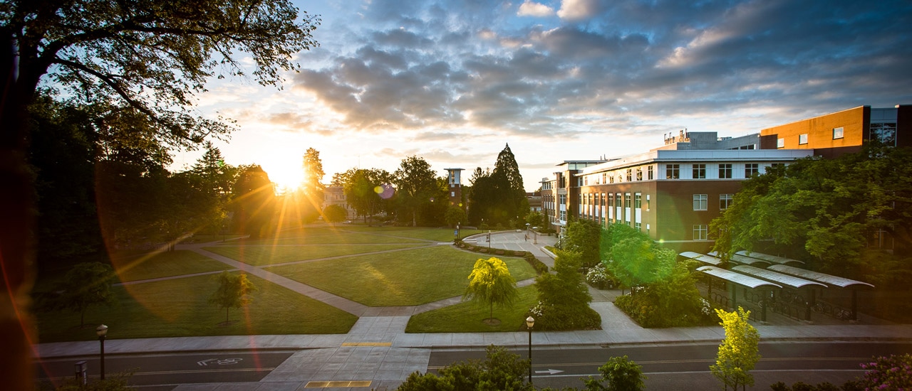 A bright sun rises over distant trees on the quad in front of Oregon State University's Valley Library.