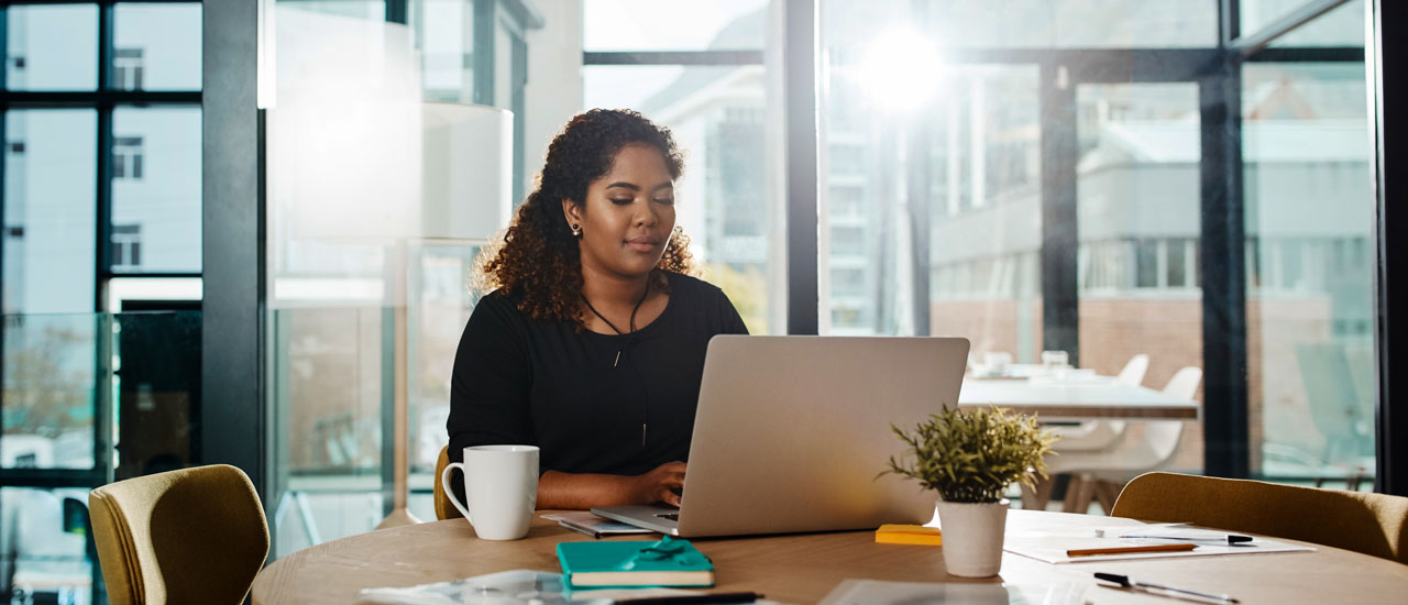 A woman working on a laptop at a round table in a modern, sunlit office