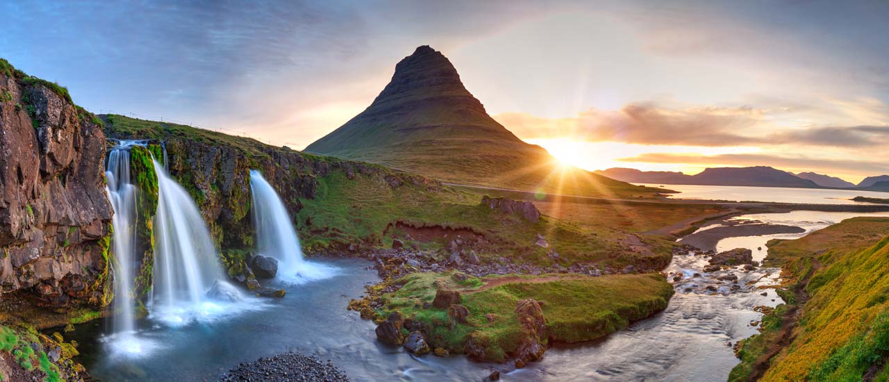 A panoramic view of Mt. Kirkjufell, a mountain in Iceland, accompanied by nearby waterfalls, near the Icelandic coast