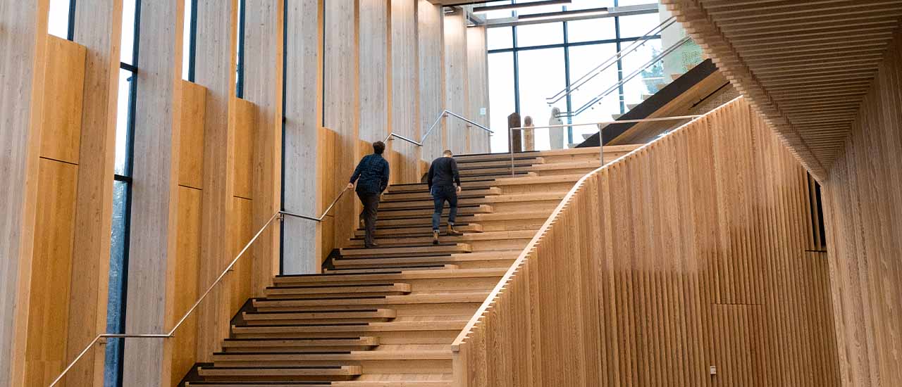 A modern OSU building interior featuring exposed mass timber, large windows, and open stair seating, showcasing innovative construction