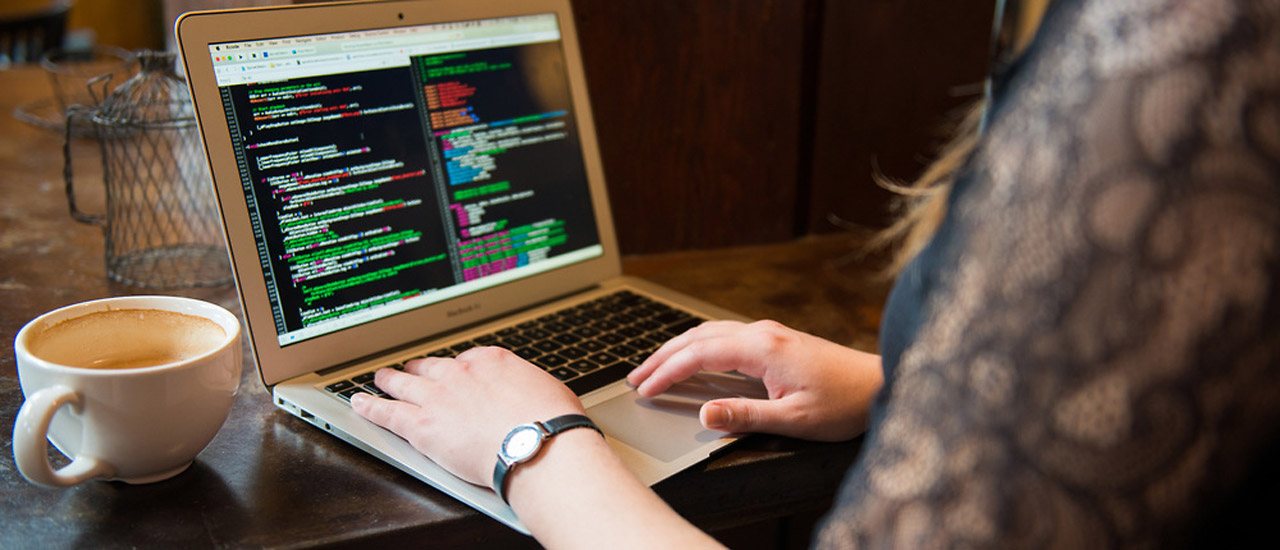 Woman reviewing code on laptop computer with cup of coffee